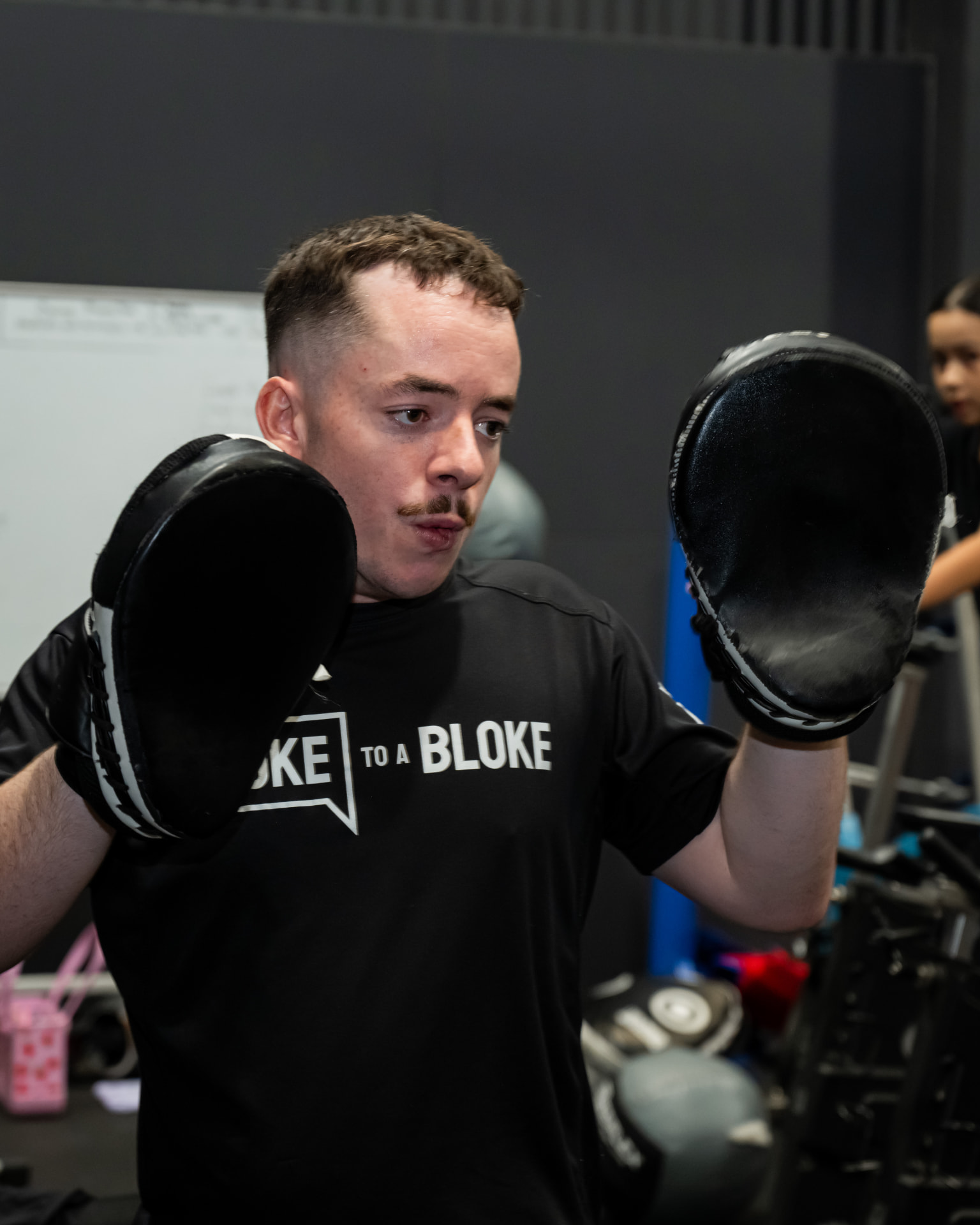 Young man in a Spoke to a Bloke shirt holding boxing pads at the gym