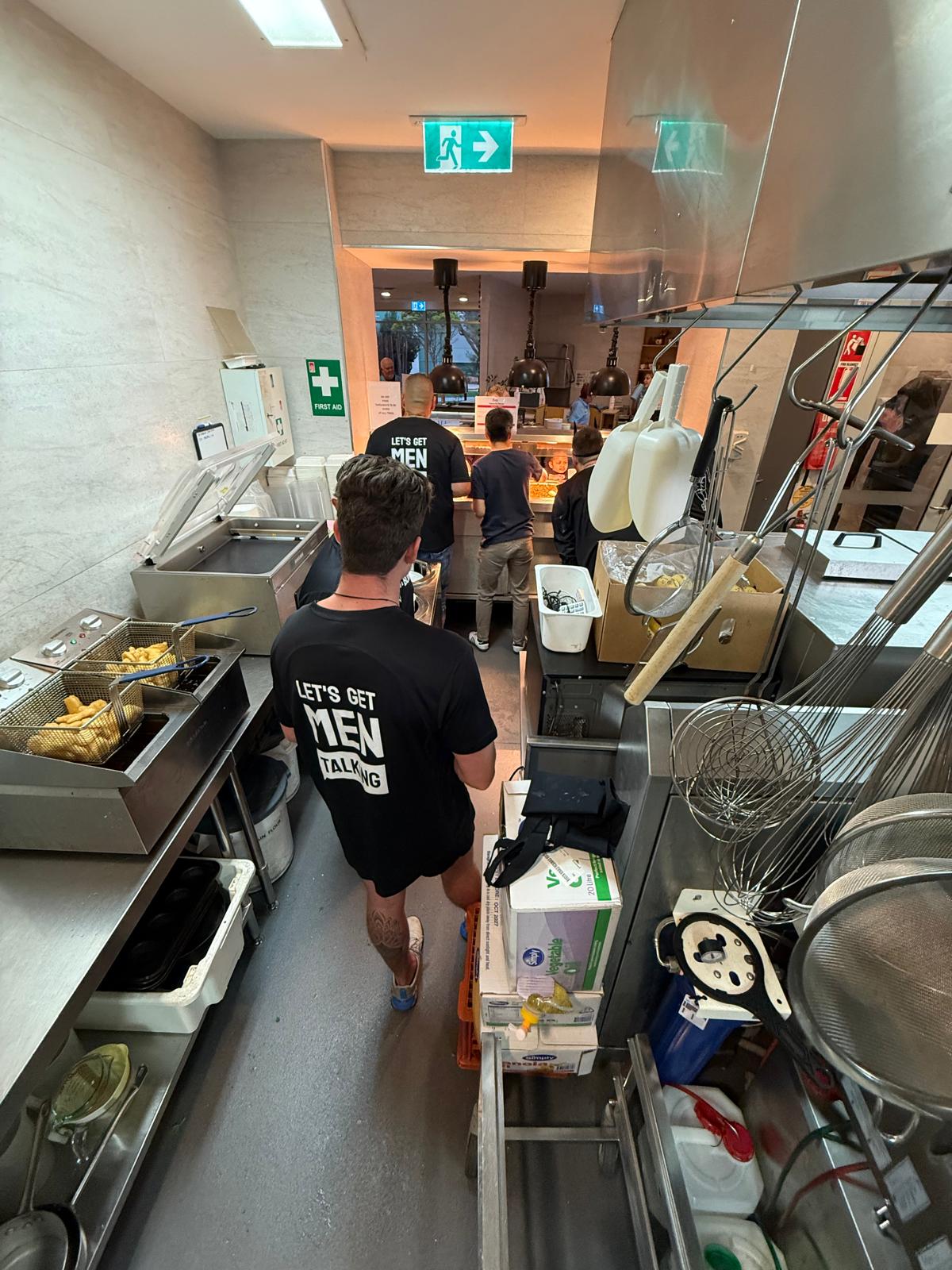 Volunteer in a Let's Get Men Talking tee wheeling supplies through the kitchen