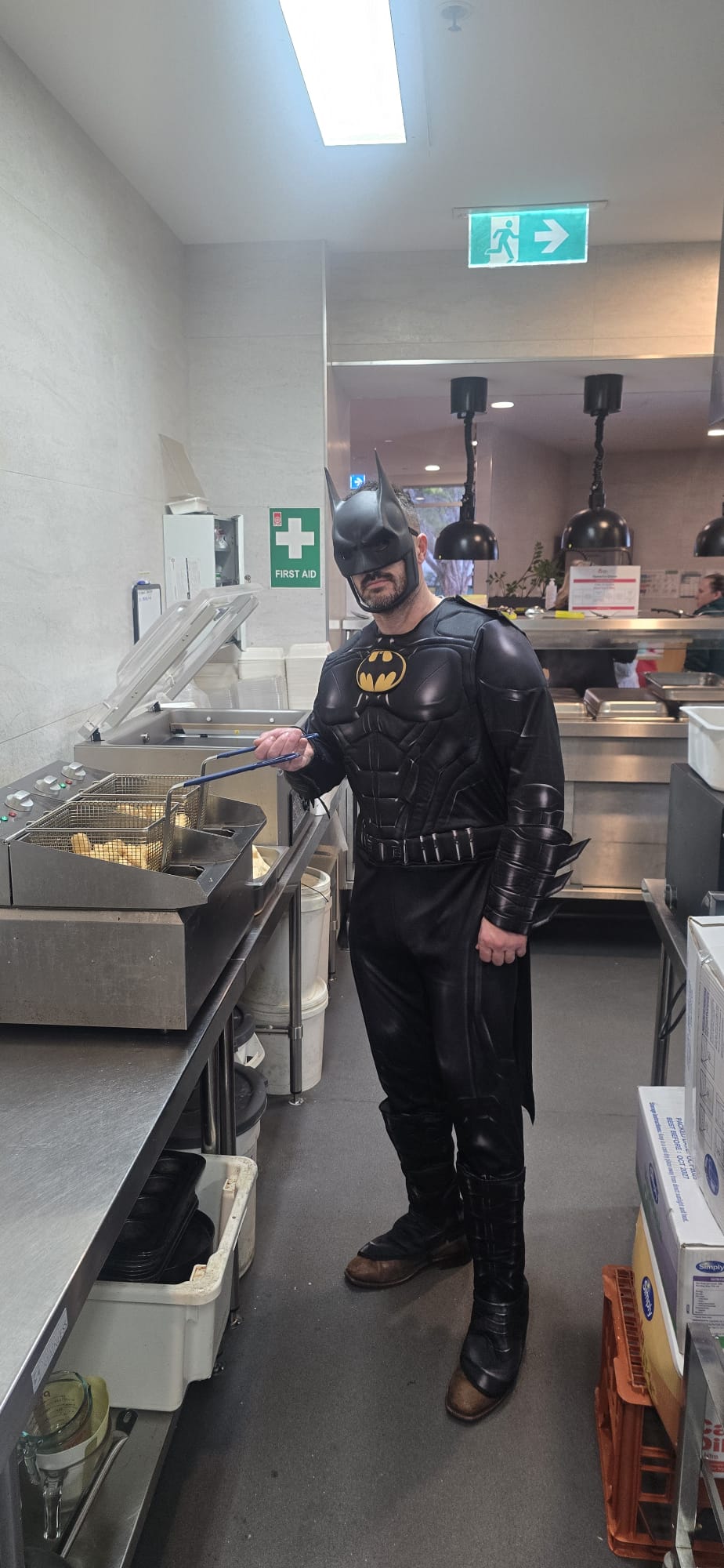 A volunteer in a Batman costume working the fryer in the kitchen