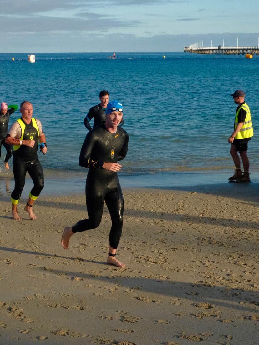 Swimmers in wetsuits running out of the ocean during an open water swim