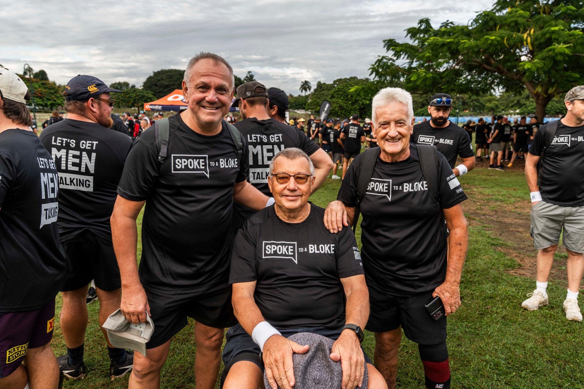 Three older men in Spoke to a Bloke shirts smiling together at a walk
