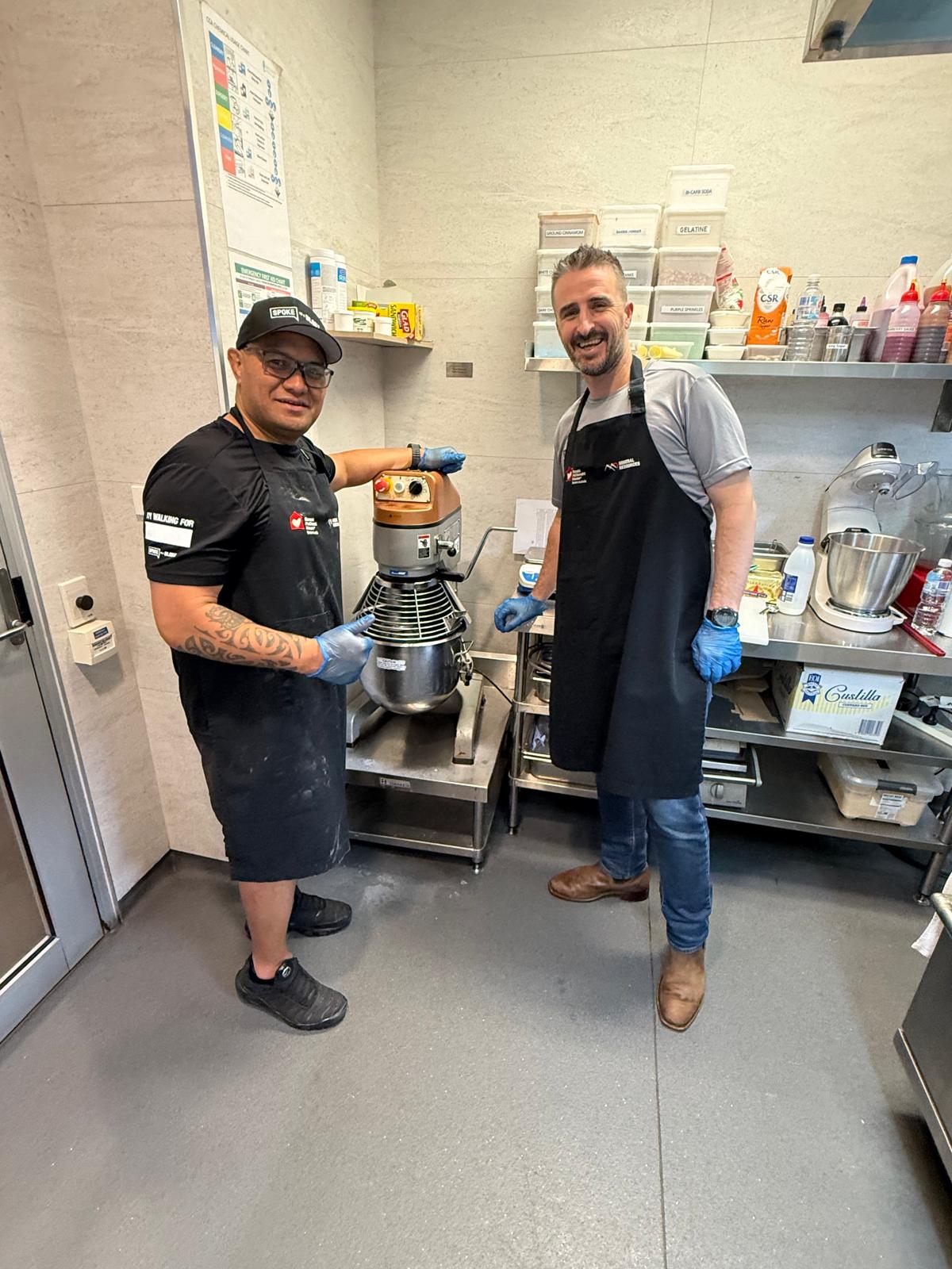 Two blokes in aprons prepping dessert with the kitchen mixer